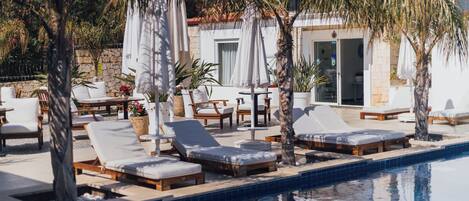 Un espace aménagé au bord de la piscine, avec des chaises longues, des parasols et un bâtiment à la façade en pierre.