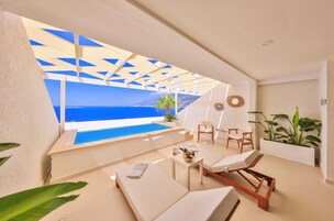 Un salón al aire libre moderno con piscina, mobiliario blanco y vistas al mar.