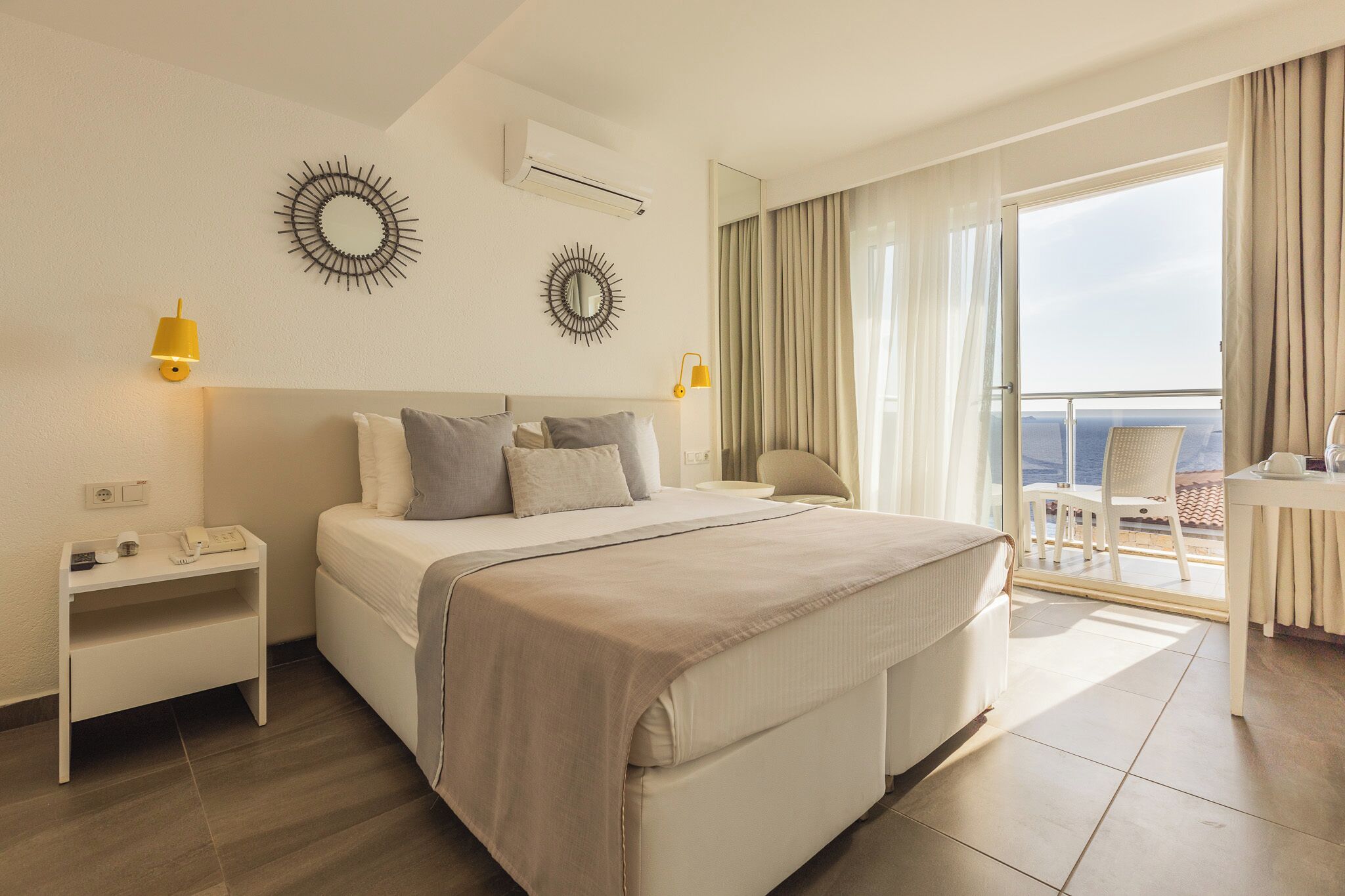 A hotel room with a bed, bedside tables, a mirror, and a balcony with a view.