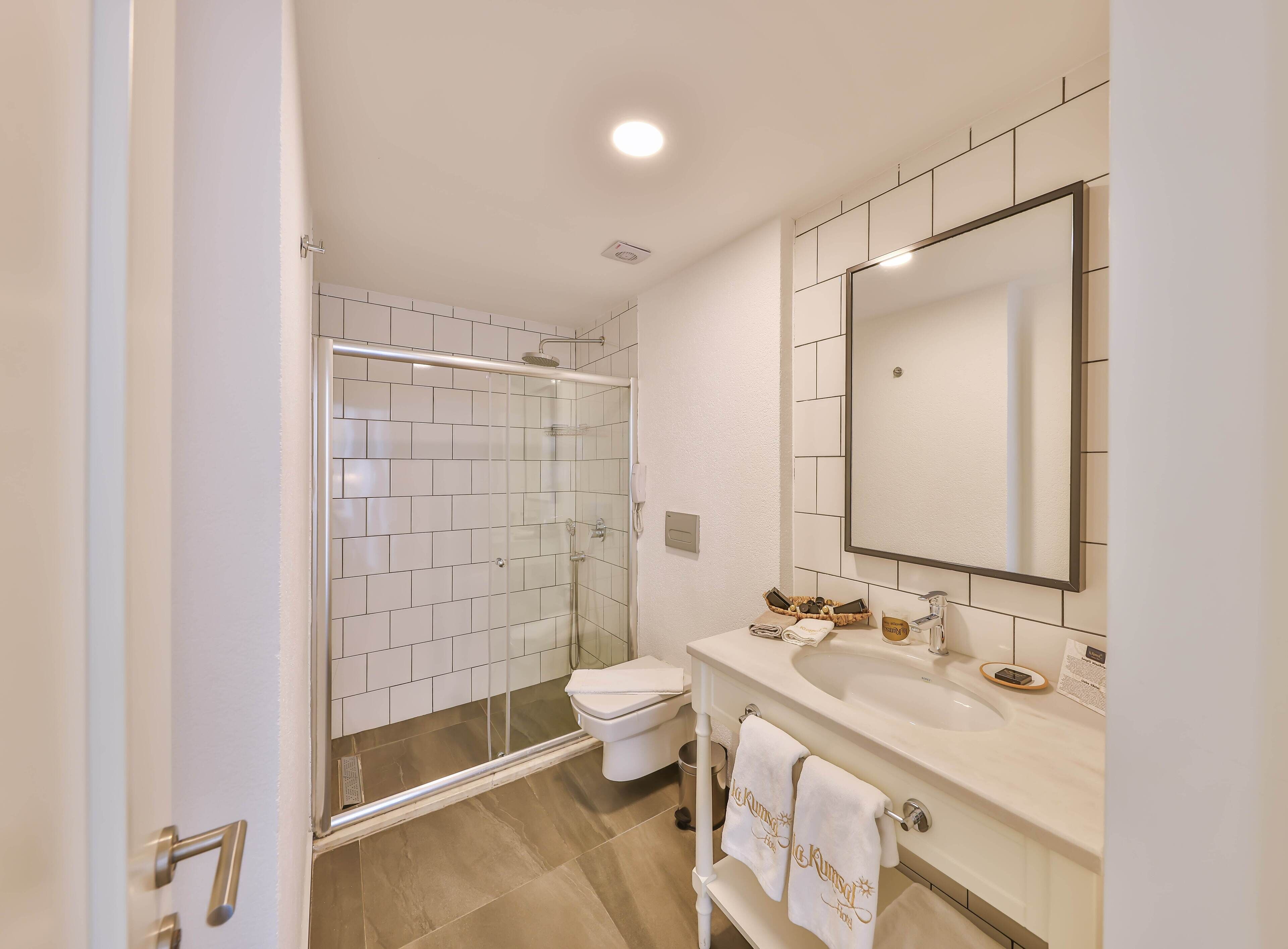 Un baño moderno con cabina de ducha de vidrio, un lavamanos blanco con un espejo grande y un inodoro.