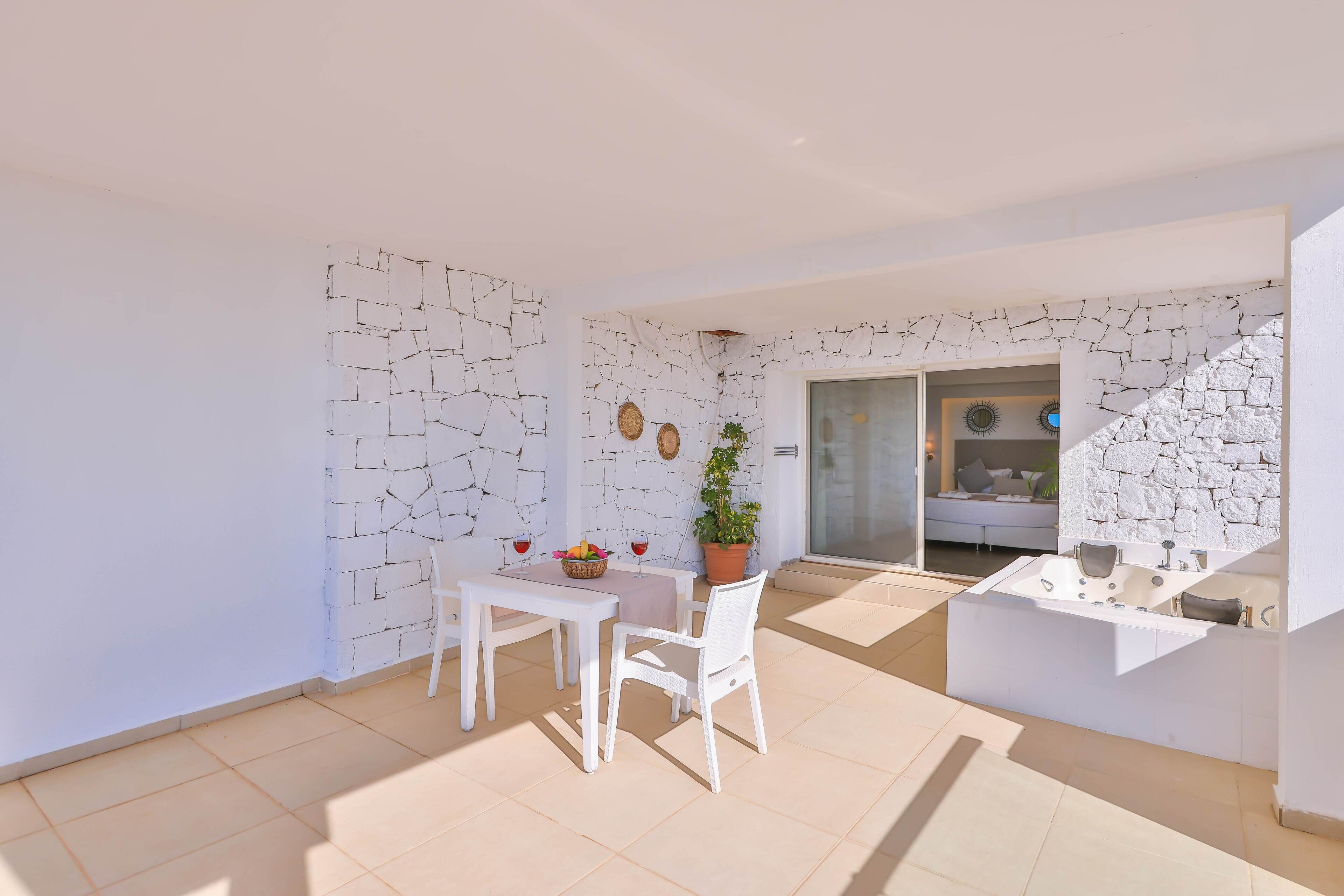 A modern apartment with a white interior, a dining area with a table and chairs, a potted plant, and a built-in bathtub.