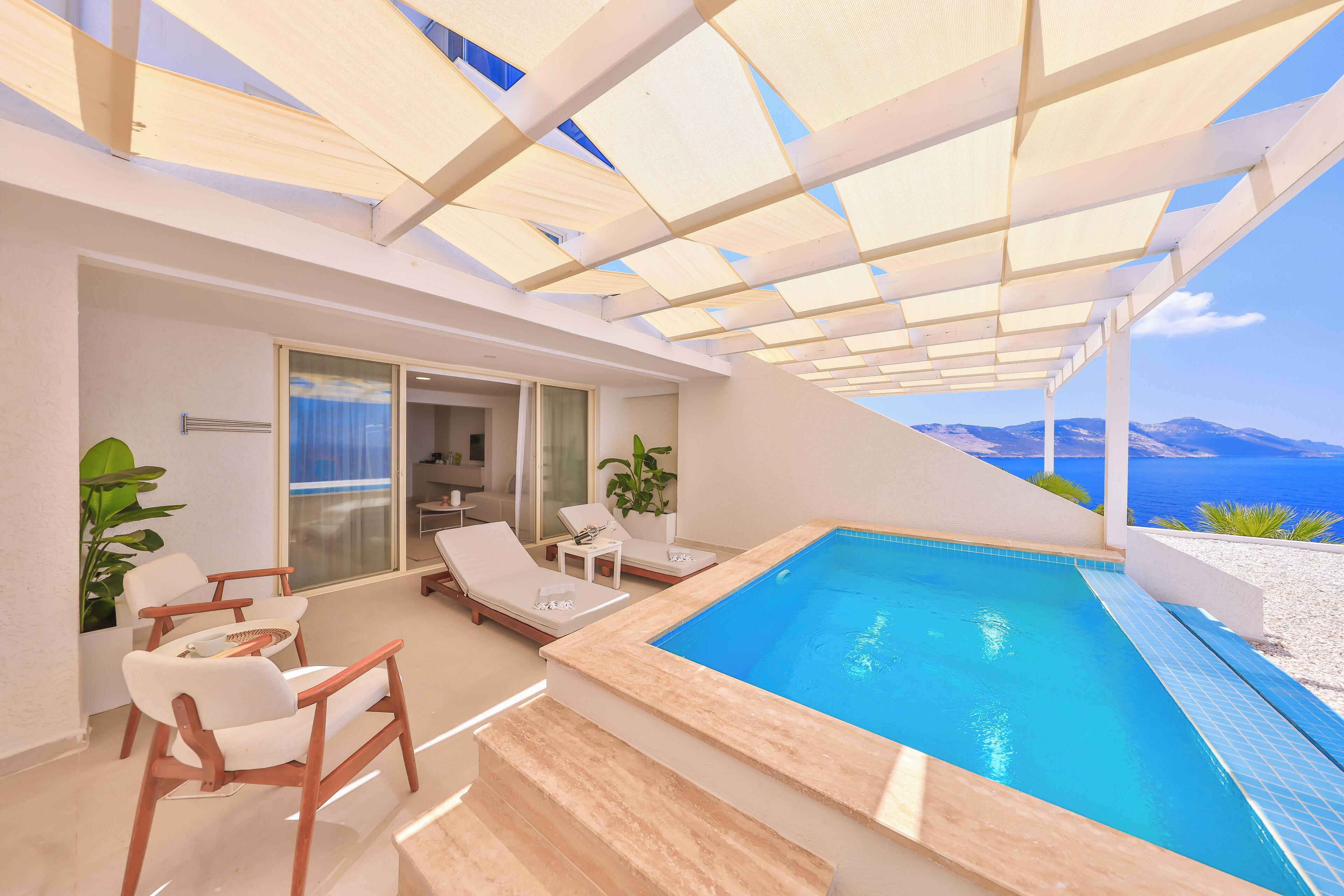 Un área de piscina moderna al aire libre con vistas despejadas al mar, sillas de descanso y una puerta de vidrio que da al interior.