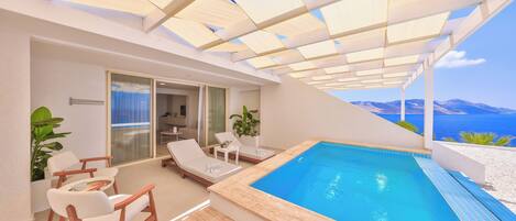 Un área de piscina moderna al aire libre con vistas despejadas al mar, sillas de descanso y una puerta de vidrio que da al interior.