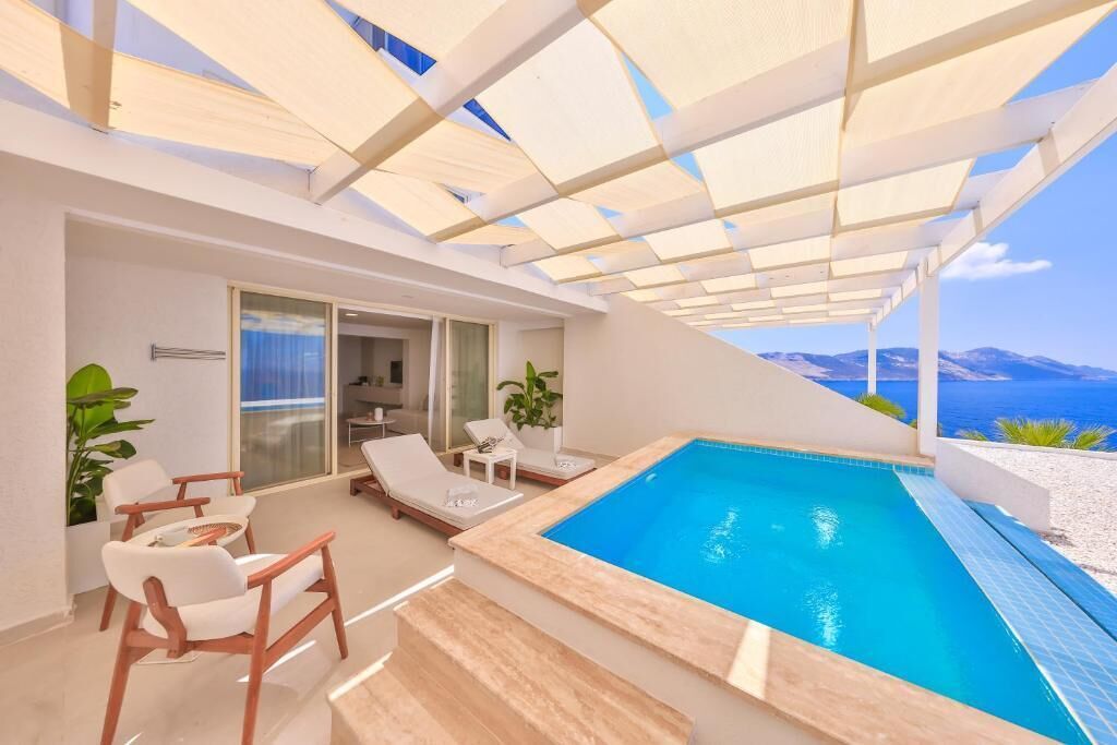 Uma área de piscina moderna ao ar livre, com vista clara para o mar, espreguiçadeiras e um espaço de estar coberto.
