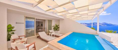 Uma área de piscina moderna ao ar livre, com vista clara para o mar, espreguiçadeiras e um espaço de estar coberto.
