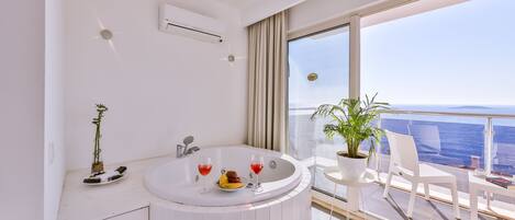 Un baño moderno con una bañera, una mesita con fruta y copas de vino, y una planta en maceta.