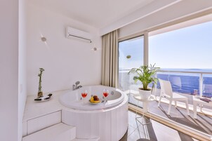 Un baño moderno con una bañera, una mesita con fruta y copas de vino, y una planta en maceta.