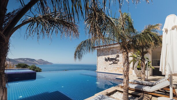 Una piscina infinita con vistas despejadas al mar, un muro de piedra con un letrero y sillas de descanso.
