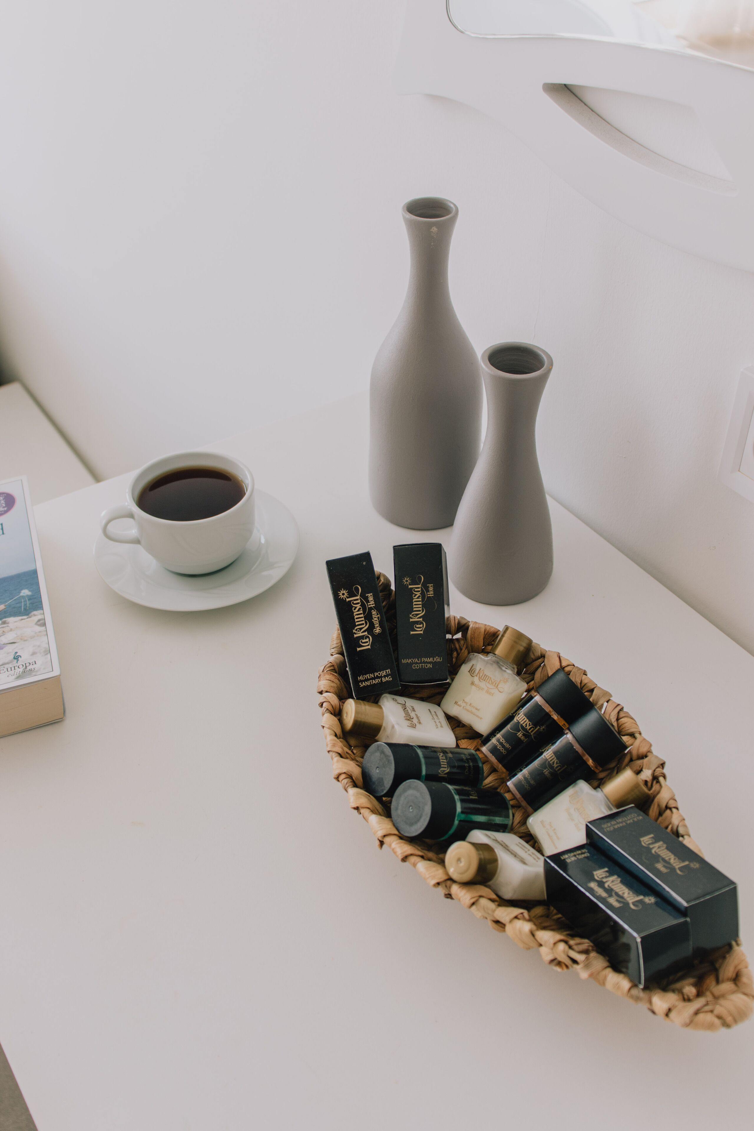 A white table with a cup of coffee, two vases, and a basket of toiletries.