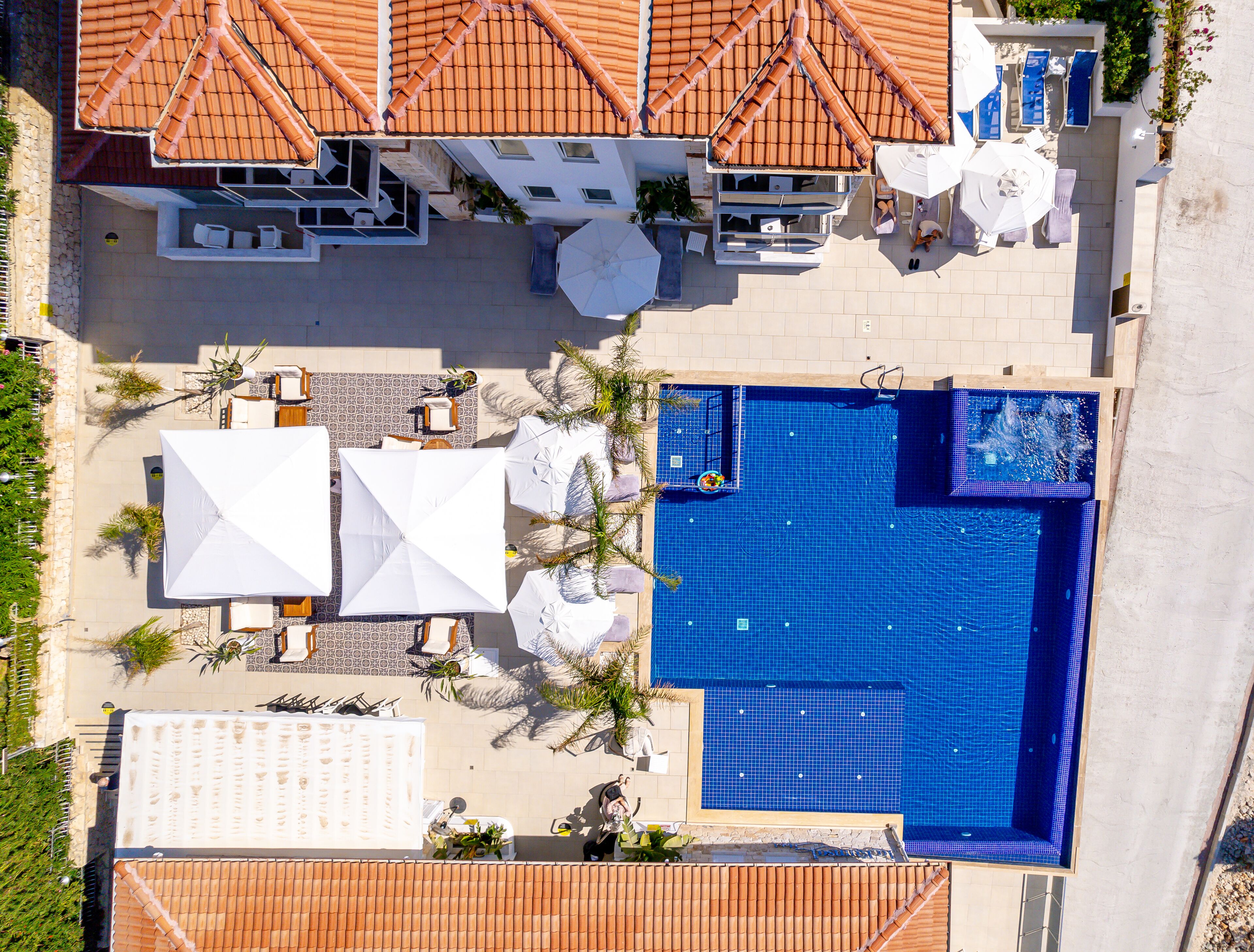 An aerial view of a hotel with a swimming pool, outdoor seating, and a tiled roof.