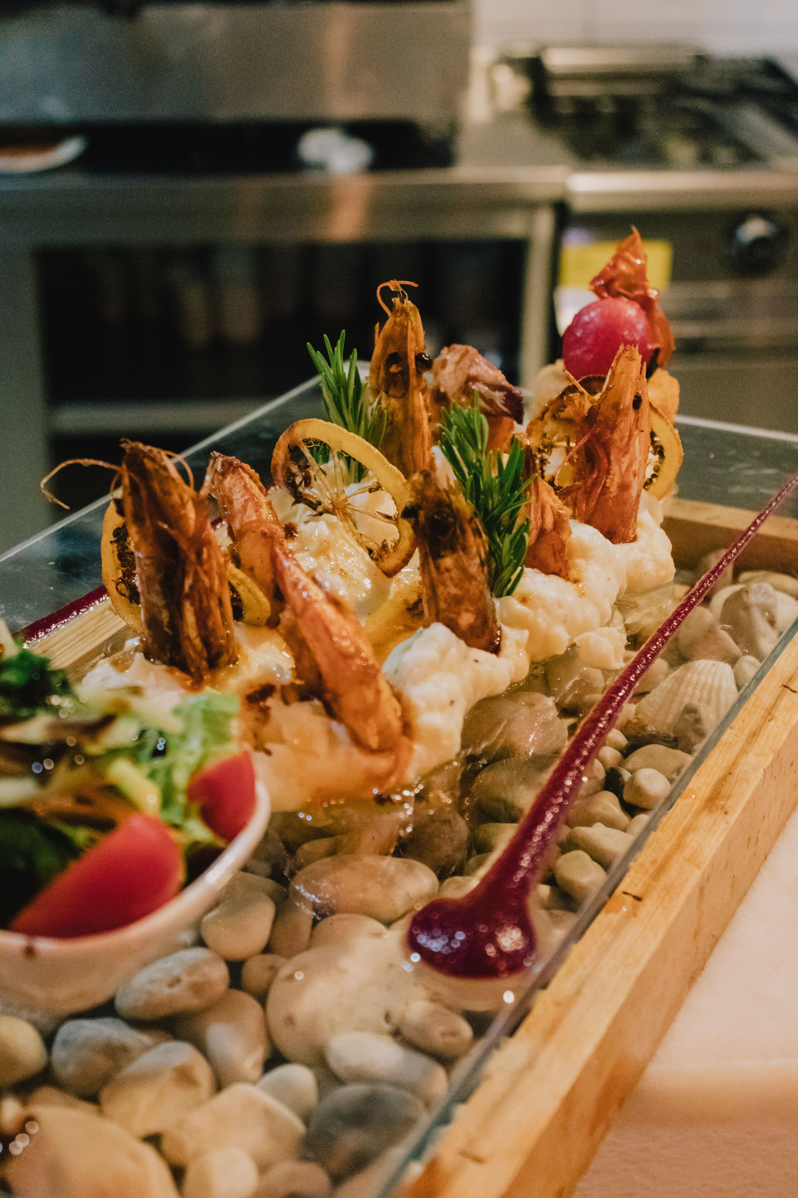 Un plateau de fruits de mer comprenant des crevettes, des coquilles Saint-Jacques et diverses garnitures, le tout disposé sur un lit de petits galets.