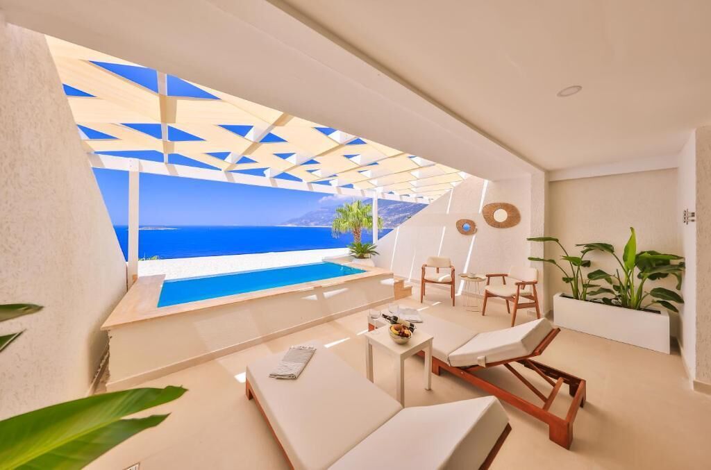 A modern outdoor lounge area with a pool, seating, and a view of the sea.