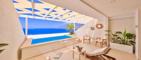 A modern outdoor lounge area with a pool, seating, and a view of the sea.