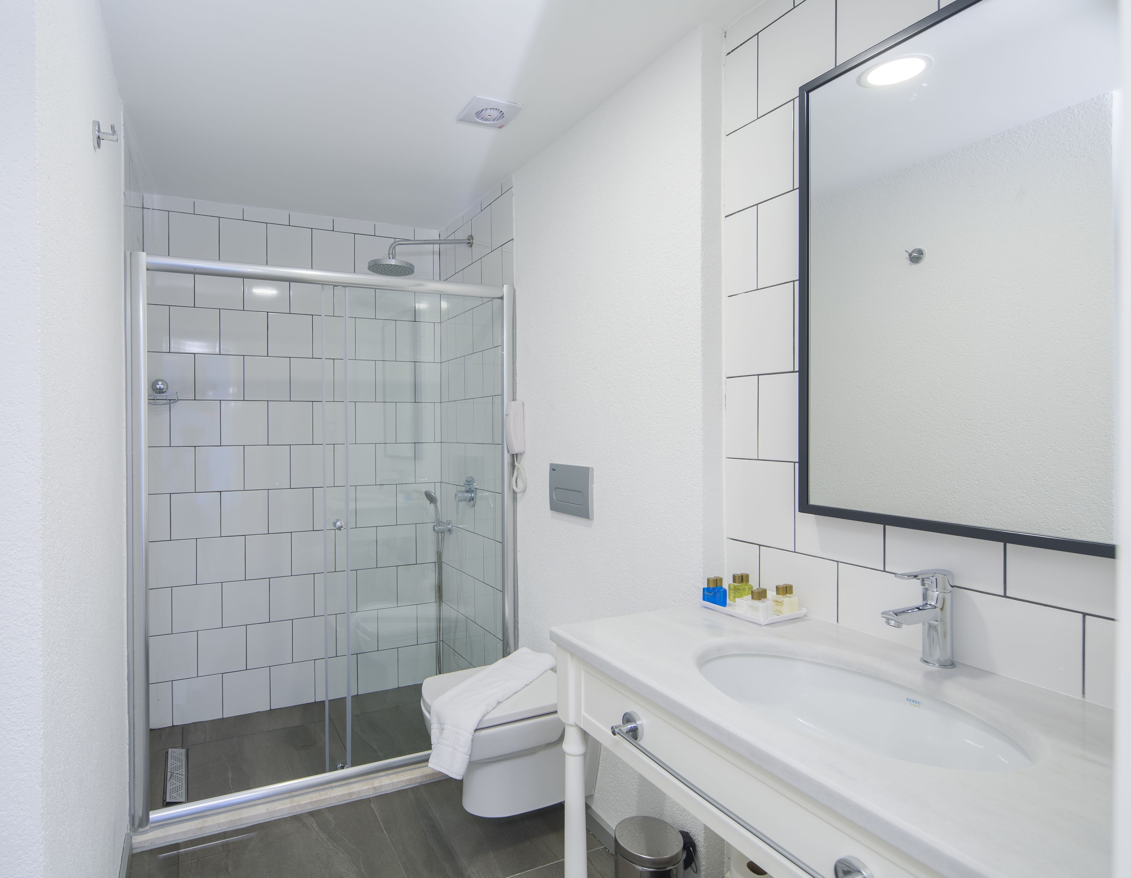 Un baño moderno con ducha de vidrio, lavamanos blanco y un espejo grande, además de un inodoro.
