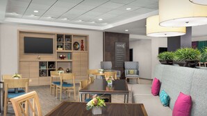 A modern hotel lobby with a dining area, seating, and a reception desk. - Home2 Suites by Hilton Knoxville West (Knoxville)