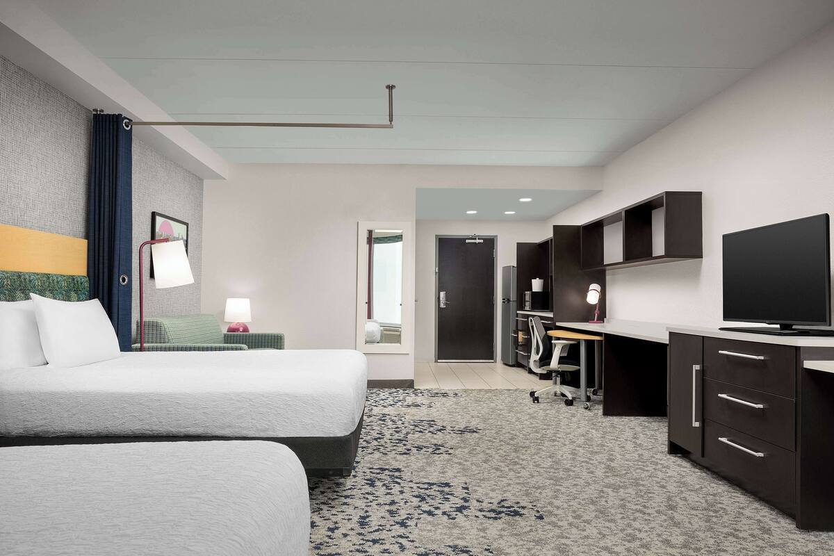 Une chambre d’hôtel avec deux lits, un bureau avec une télévision et une armoire.