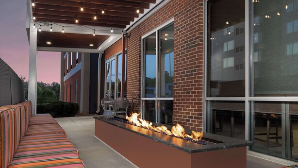 A covered outdoor seating area with a fire feature and a bench with colorful stripes. - Home2 Suites by Hilton Knoxville West (Knoxville)