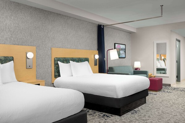 A hotel room with two beds, a large mirror, a nightstand, and a red ottoman.