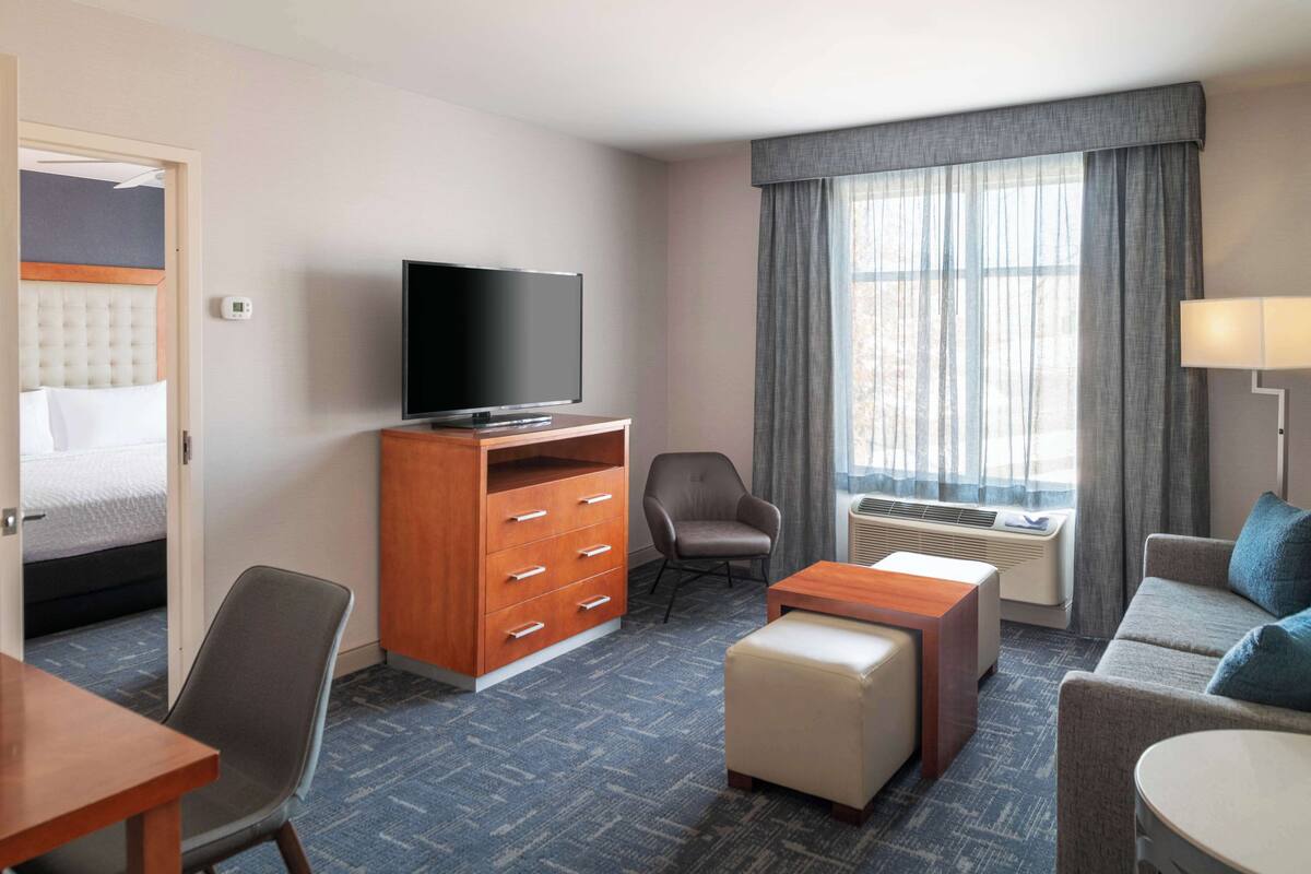 Een hotelkamer met een bed, een televisie, een bureau, een stoel, een bank en een raam met gordijnen.