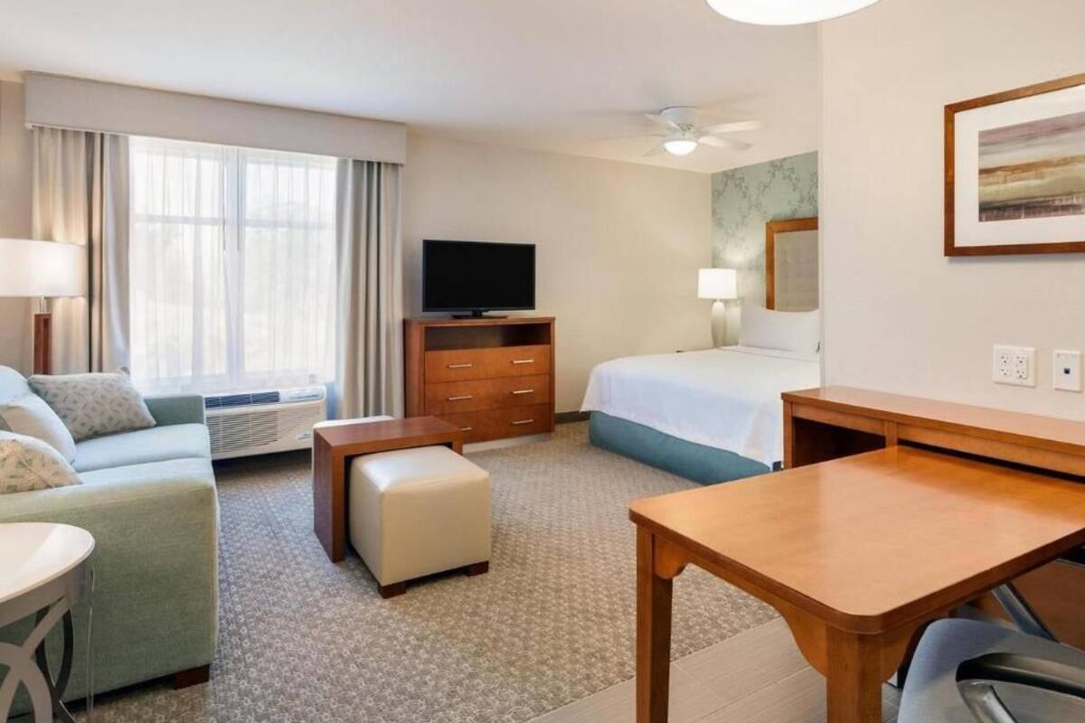 Een hotelkamer met een bed, een bureau, een televisie, een bank en een raam met gordijnen.