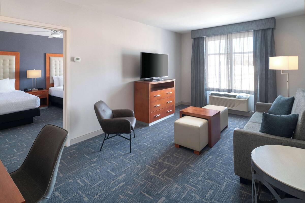 Hotelkamer met een bed, bureau, stoel, bank, televisie en raam met gordijnen.