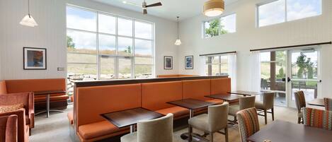 Un comedor moderno con techos altos, ventanas amplias y una variedad de opciones de asientos, incluyendo mesas y cabinas.