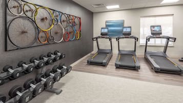 Un gimnasio con cintas de correr, mancuernas y una obra de arte con una rueda de bicicleta en la pared.
