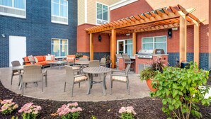 Een terras buiten met rieten meubilair, een barbecue en een pergola.