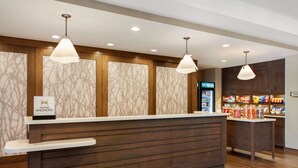 Een receptiegedeelte met een houten receptiebalie, twee hanglampen, een minibars en een digitaal scherm.
