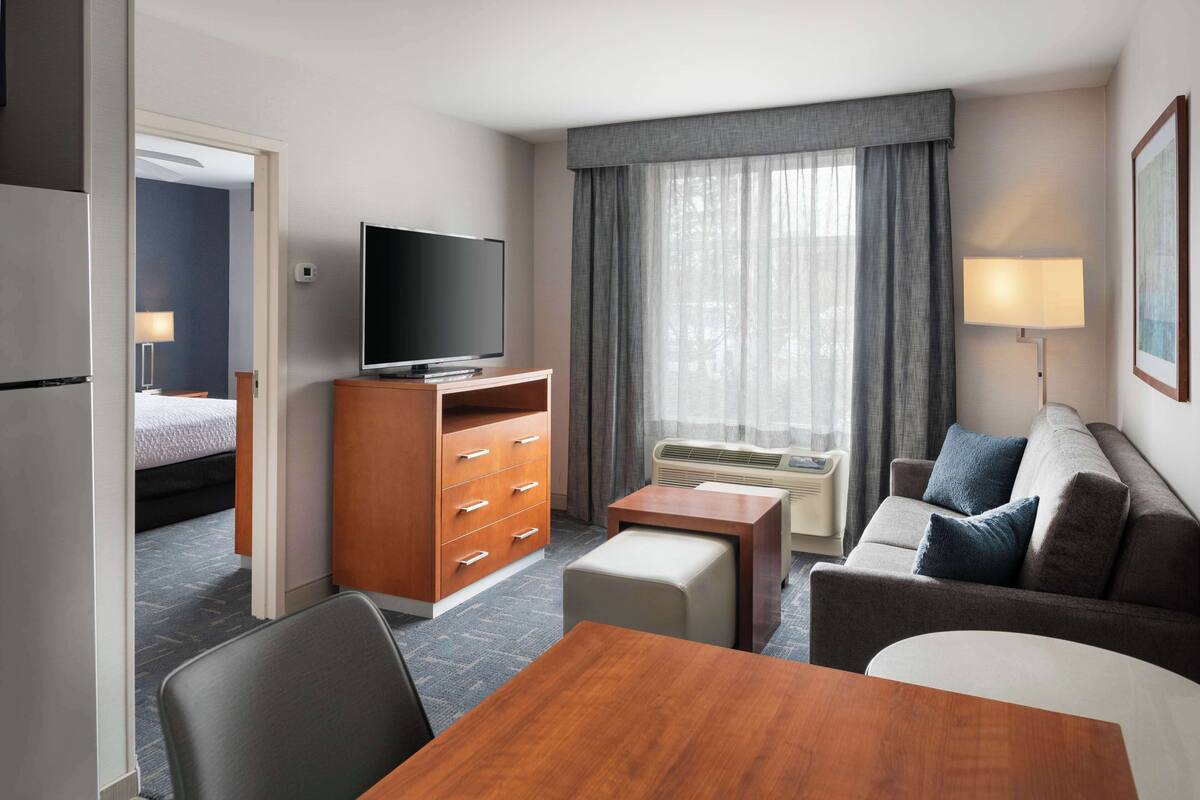 Een hotelkamer met een houten bureau, een televisie, een sofa, een klein tafeltje en een raam met gordijnen.