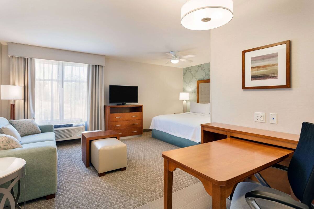 Een hotelkamer met een bed, bureau, bank, televisie en een raam met gordijnen.