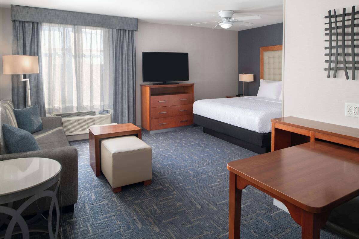 Een hotelkamer met een bed, een televisie, een bureau, een stoel, een bank en een raam met gordijnen.