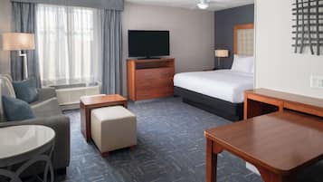 Habitación de hotel con cama, televisión, escritorio, silla, sofá y ventana con cortinas.