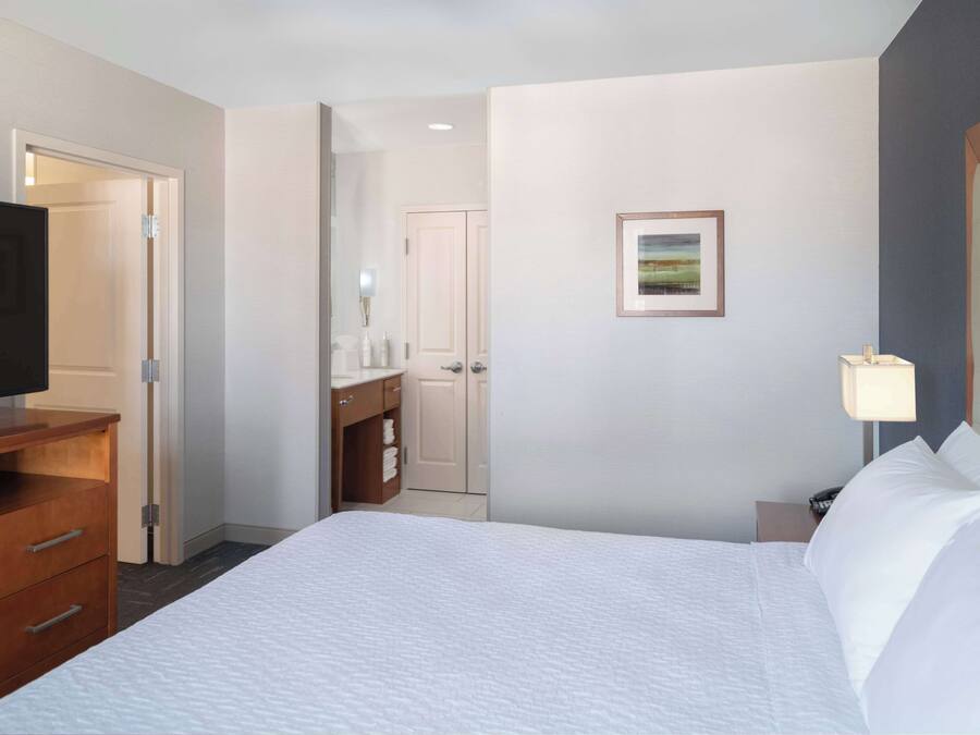 A hotel room with a bed, a TV, a desk, and a bathroom visible through an open door.