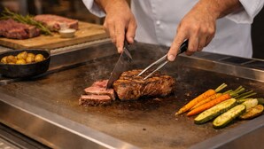 Un chef cortando filete en una parrilla, con verduras cerca.