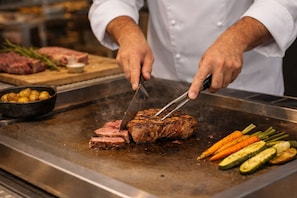 Ein Koch schneidet Steak auf einem Grill, Gemüse in der Nähe.