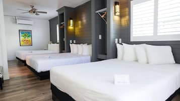 A hotel room with three beds, a ceiling fan, and a large window with blinds.