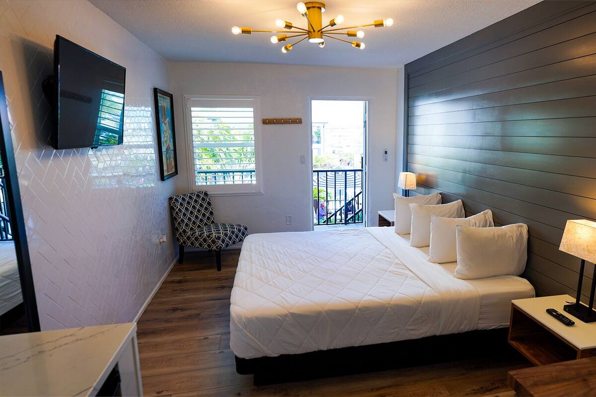 Un dormitorio con cama, mesitas de noche, una silla, televisor y balcón con vistas.