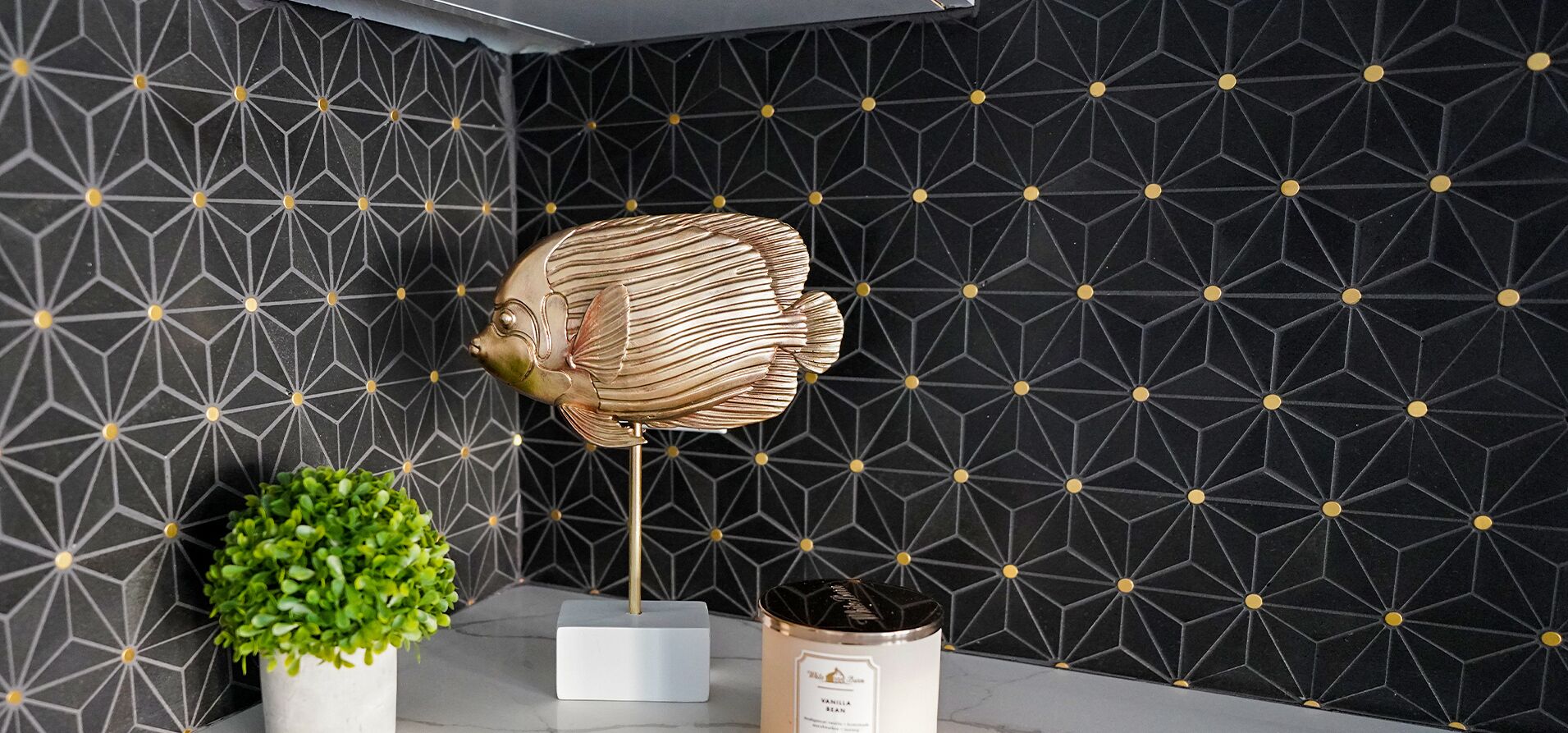 A modern interior with a geometric patterned wall, a decorative fish sculpture, a small green plant, and a container labeled "Vanilla Bean."