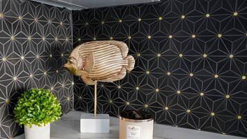 A modern interior with a geometric patterned wall, a decorative fish sculpture, a small green plant, and a container labeled "Vanilla Bean."