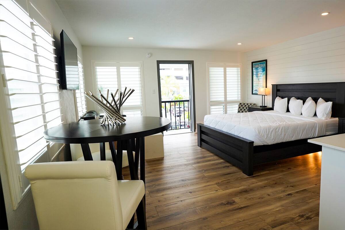 Un dormitorio moderno con una cama grande, un escritorio y una silla. Hay un balcón con vistas al exterior.