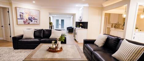 A living room with two black leather sofas, a coffee table with decorative items, and a painting on the wall.