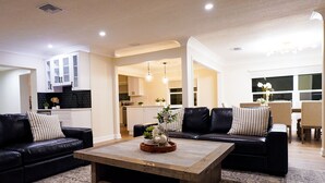 Una sala de estar moderna con sofás de cuero negro, una mesa de centro de madera y una cocina al fondo.