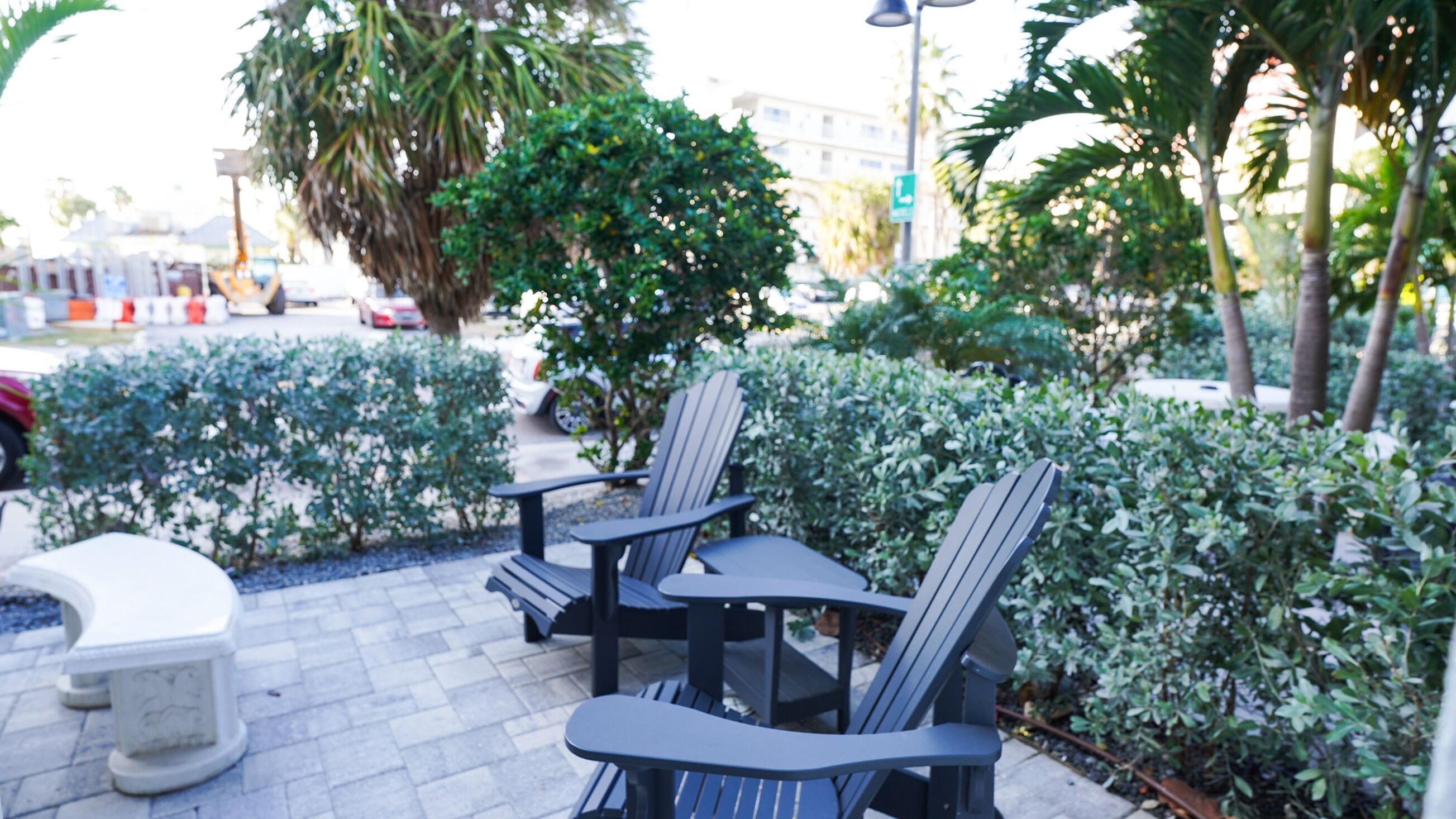 An outdoor seating area with a table and chairs, surrounded by greenery and a paved walkway.