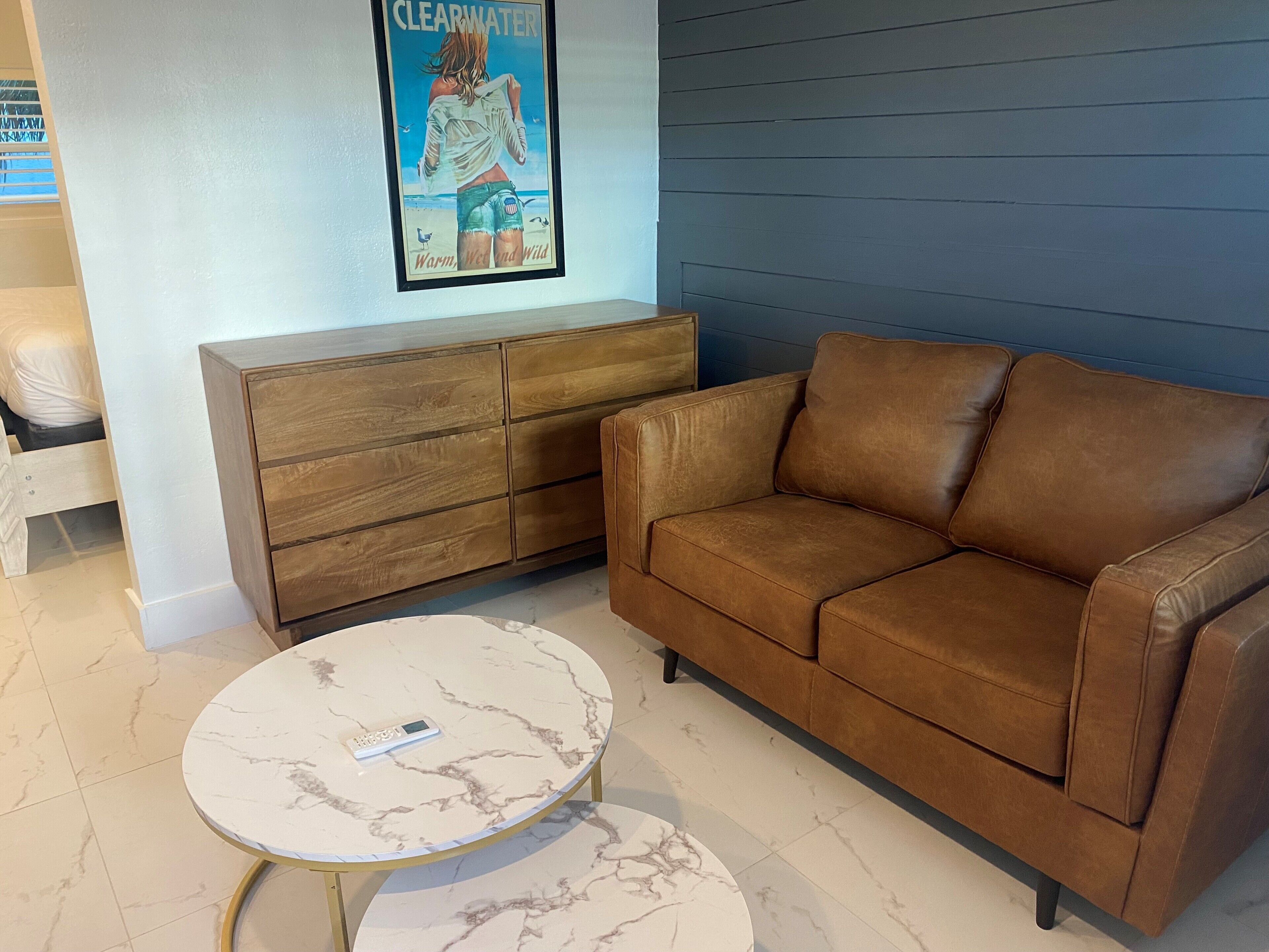 A brown leather sofa, a wooden cabinet, and a marble table with a remote control.