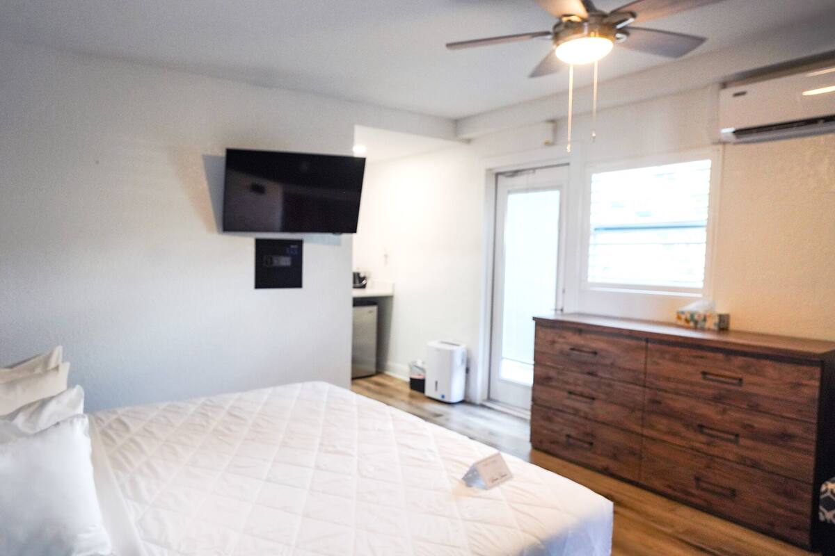 Un dormitorio con una cama, un televisor montado en la pared, un aparador y un ventilador de techo.
