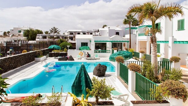 Uma área de piscina com piscina azul cristalina, espreguiçadeiras e uma palmeira.