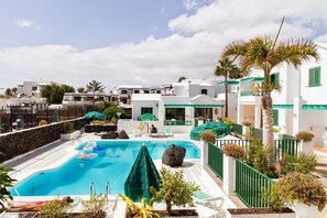 A pool area with a clear blue pool, lounge chairs, and a palm tree. - Apartamentos las Acacias (Tías)