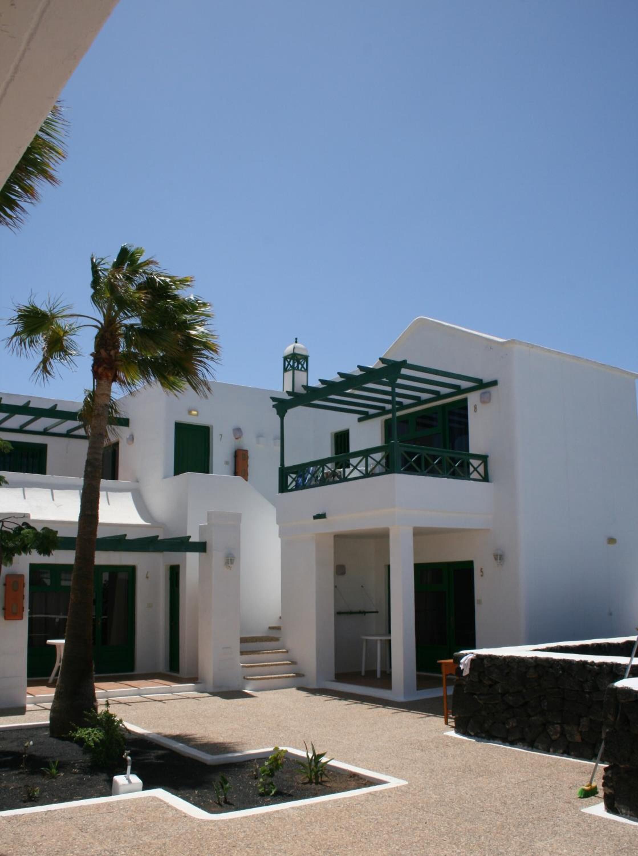 A white building with green accents, a staircase, and a palm tree.