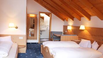 A hotel room with two beds, a small table, a bench, and a bathroom visible through an open door.
